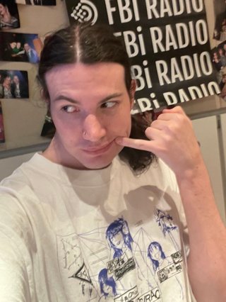 A selfie of Jim in the fbi studio, with their pinky to the corner of their mouth and their gaze to the side.