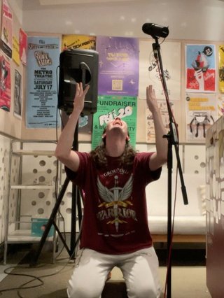 Jim in the studio on their knees, with their hands raised to the sky.