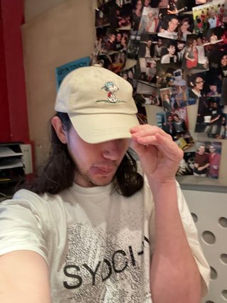 A selfie of Jim in the studio. They are pulling their cap down over their face and sticking out their tongue.