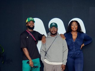 CMJ, OVO and MC Q stand together against a dark blue wall with a white graphic. They are gazing confidently at the camera, arms resting on each other's shoulders.