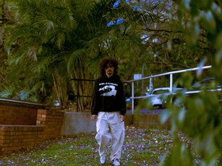 Miles Nautu stands in a suburban garden in the evening. There are purple flowers littered all over the grass around him,