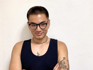 Against a white background, Matt Do wears a black tank top, black glasses and has is arms crossed smiling while looking to his right.