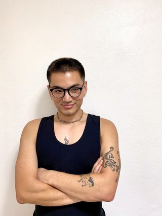 Against a white background, Matt Do wears a black tank top, black glasses and has is arms crossed smiling while looking to his right.