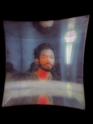 Wharped square tile containing an artistic rendering of Toro Y Moi against a black background. Lit in red light