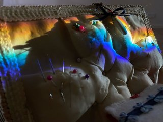 A piece of fabric is pierced by sewing pins with different coloured heads, a rainbow light is cast on the fabric