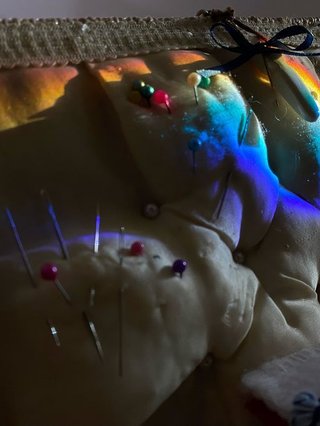 A piece of fabric is pierced by sewing pins with different coloured heads, a rainbow light is cast on the fabric