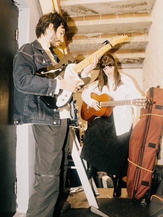 Jerome Blaze and Sarah Levins Playing guitars in a concrete hall